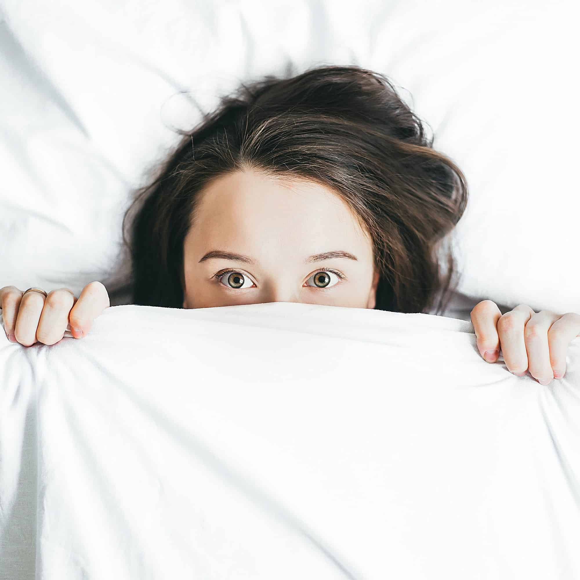 Woman hiding under a blanket with fear in her eyes