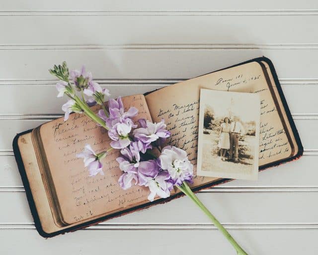 Old diary with text, a picture of a couple and white/purple flower over the top